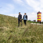 Zwei Wanderer an der Nordsee vor Leuchtturm